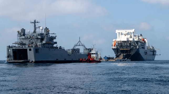 A deep-draft Military Sealift Command ro/ro transloads rolling cargo onto an Army landing craft at a moored transfer platform off Gaza, 2024 (USN)