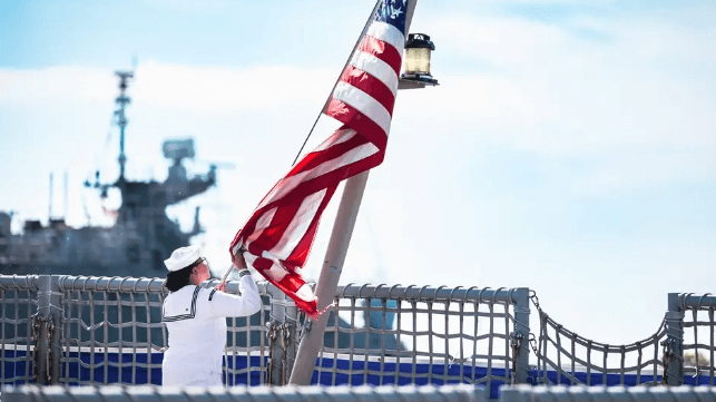 A member of USS Sioux City's crew lowers the ensign for the final time (USN)