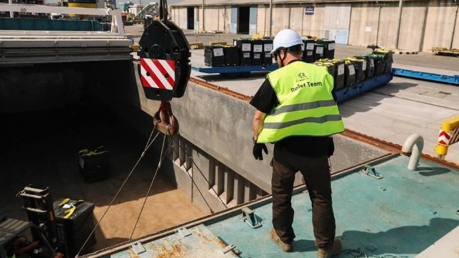 An aid worker helps load food cargo aboard a small freighter chartered by World Central Kitchen (WCK)