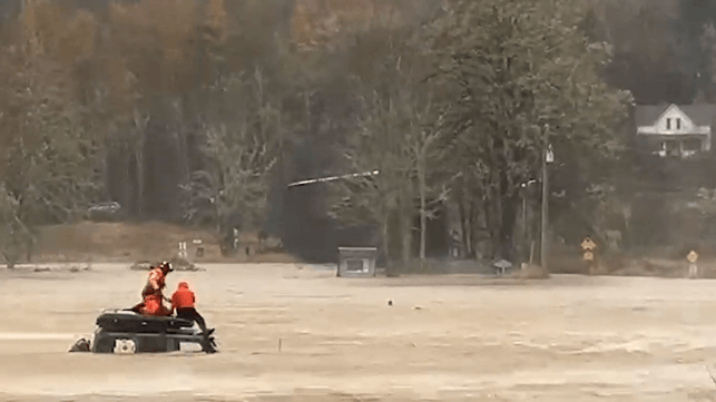 Rescue swimmer retrieving man from on top of car amidst flooding