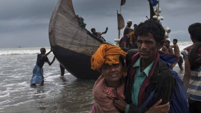 Rohingya refugees disembarking a wooden boat in surf on a beach